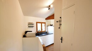 Un escalier étroit mène à une cuisine avec des poutres en bois, des murs blancs et une porte en bois.