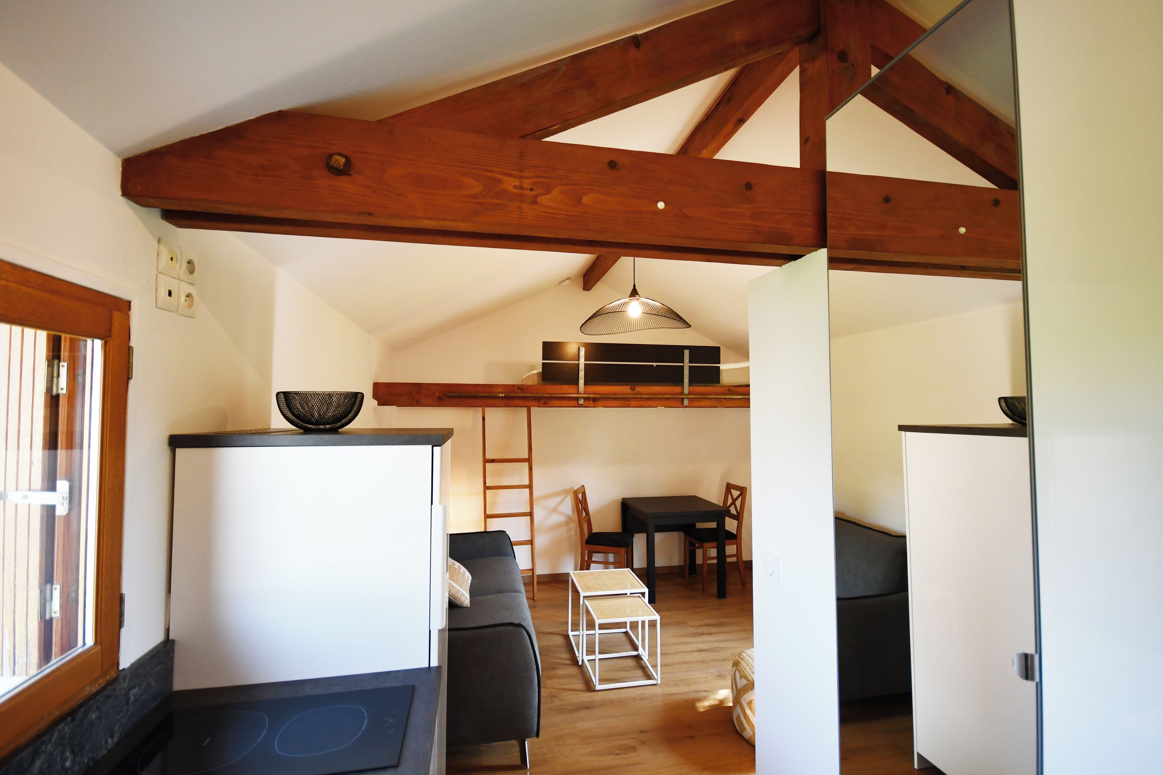 Un espacio habitable compacto con kitchenette, un sofá, una mesa de comedor y un techo con vigas de madera a la vista.