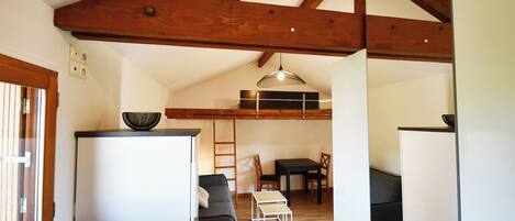 Un espacio habitable compacto con kitchenette, un sofá, una mesa de comedor y un techo con vigas de madera a la vista.