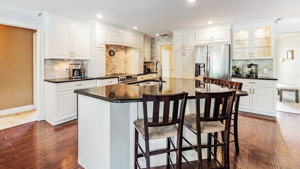 A spacious kitchen with white cabinetry, a large island with bar stools, stainless steel appliances, and a clock on the wall.