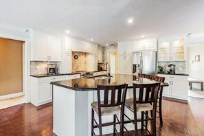 A spacious kitchen with white cabinetry, a large island with bar stools, stainless steel appliances, and a clock on the wall. - Clearwater Pool Home - Family Friendly! (Clearwater)