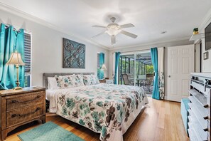 Une chambre à coucher comprenant un lit, une table de chevet, une lampe, un ventilateur de plafond et une vue sur l’extérieur grâce à une porte vitrée.