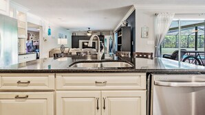 A modern kitchen with white cabinetry, a stainless steel sink, and a large window overlooking a pool.