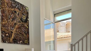 A modern living room with a large abstract painting, a black chair, a small table with a vase and candle, and a staircase leading to an outdoor area. - Duplex le Saint Paul Avec vue sur les Arènes Darles (Arles)