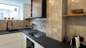 A modern kitchen with a black countertop, white cabinets, and a window providing natural light. - Duplex le Saint Paul Avec vue sur les Arènes Darles (Arles)