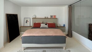 A modern bedroom with a large bed, a bedside table, a nightstand, a mirror, and a view of the outside. - Duplex le Saint Paul Avec vue sur les Arènes Darles (Arles)