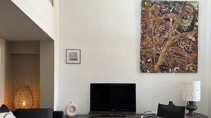 A modern living room with a sectional sofa, a coffee table, a TV, and a large abstract painting. - Duplex le Saint Paul Avec vue sur les Arènes Darles (Arles)