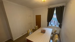A dining area with a table and chairs, a window with curtains, and a door leading to another room. - a Quiet Semi Rural Property Located in Bolsover (Chesterfield)