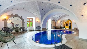 Ein Pool mit geschwungener Form, umgeben von gewölbten Decken und Sterndekorationen. Liegestühle und ein gefliester Boden sind vorhanden.