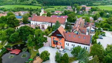 An aerial view of a village with traditional architecture, a church, and a pond with a bridge.