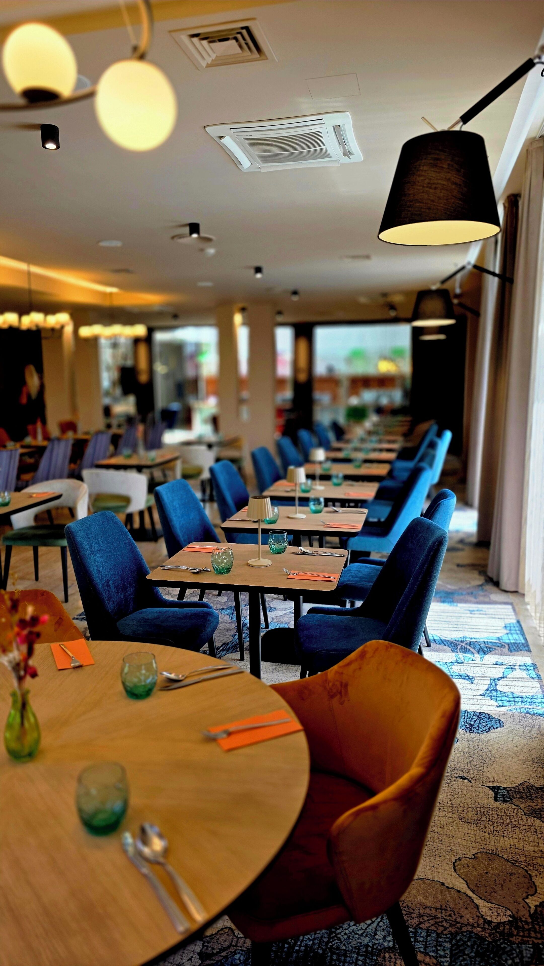 Un restaurante con mesas y sillas, una lámpara colgante y una alfombra estampada.