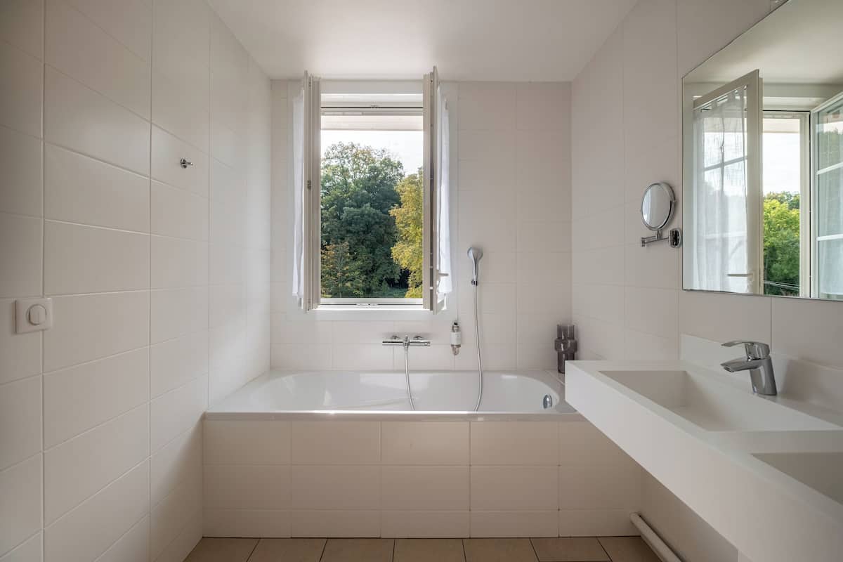 Ein modernes Badezimmer mit einer freistehenden Badewanne, einem großen Fenster und einem Waschtisch mit Spiegel.