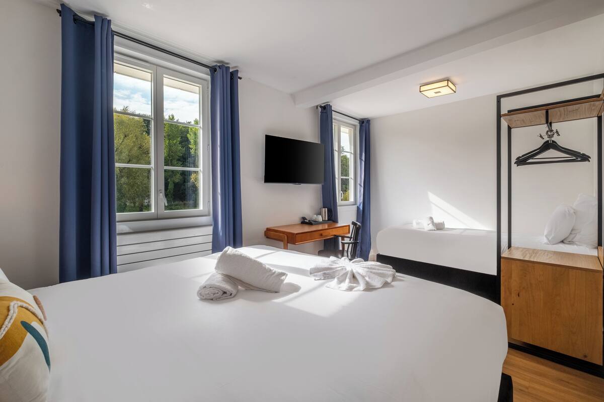 Ein Hotelzimmer mit einem großen Bett, einem Holztisch, einem Fernseher und einem Schrank mit Spiegel.
