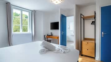 Habitación de hotel con una cama grande, un escritorio con silla, televisión, armario y baño visible a través de una puerta abierta.