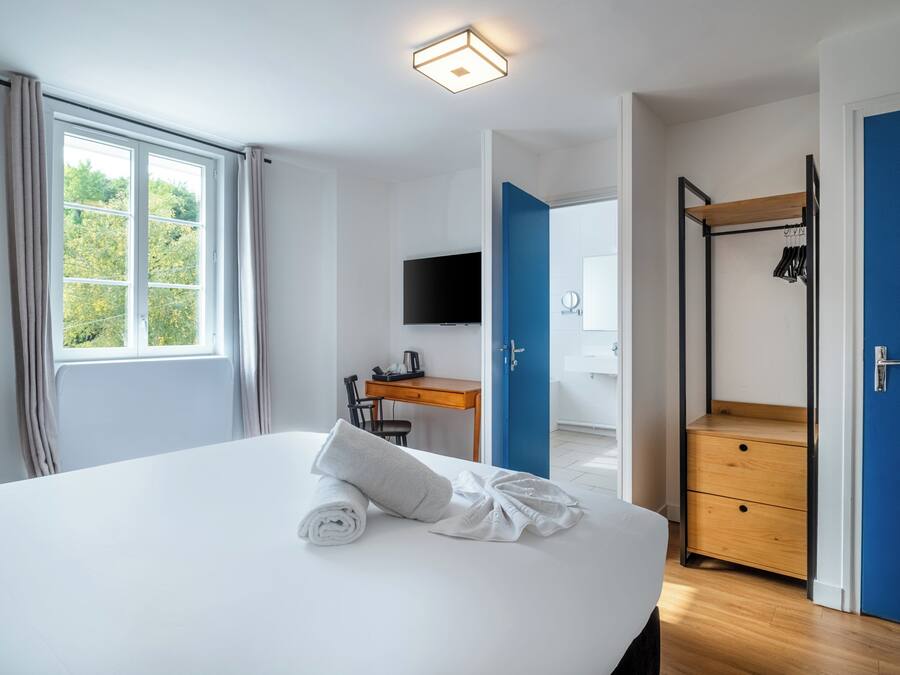 Habitación de hotel con una cama grande, un escritorio con silla, televisión, armario y baño visible a través de una puerta abierta.