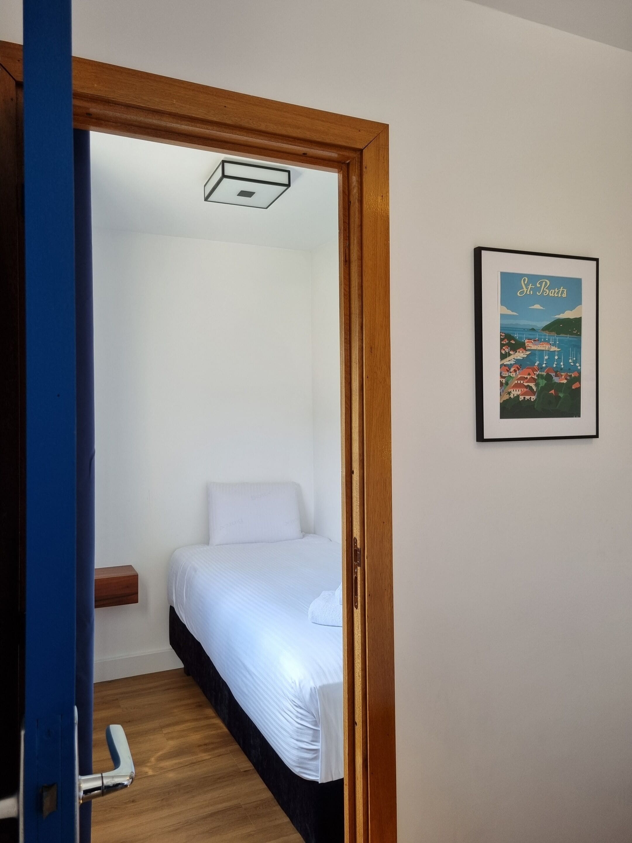 A bedroom with a bed, a wooden door frame, a small shelf, and a framed picture on the wall.
