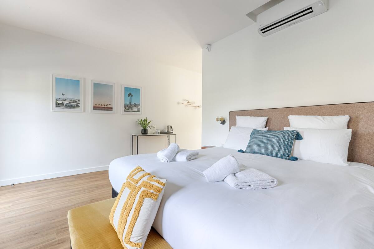 Ein modernes Hotelzimmer mit einem großen Bett, weißen Leinentüchern, Holzboden und drei gerahmten Bildern an der Wand.