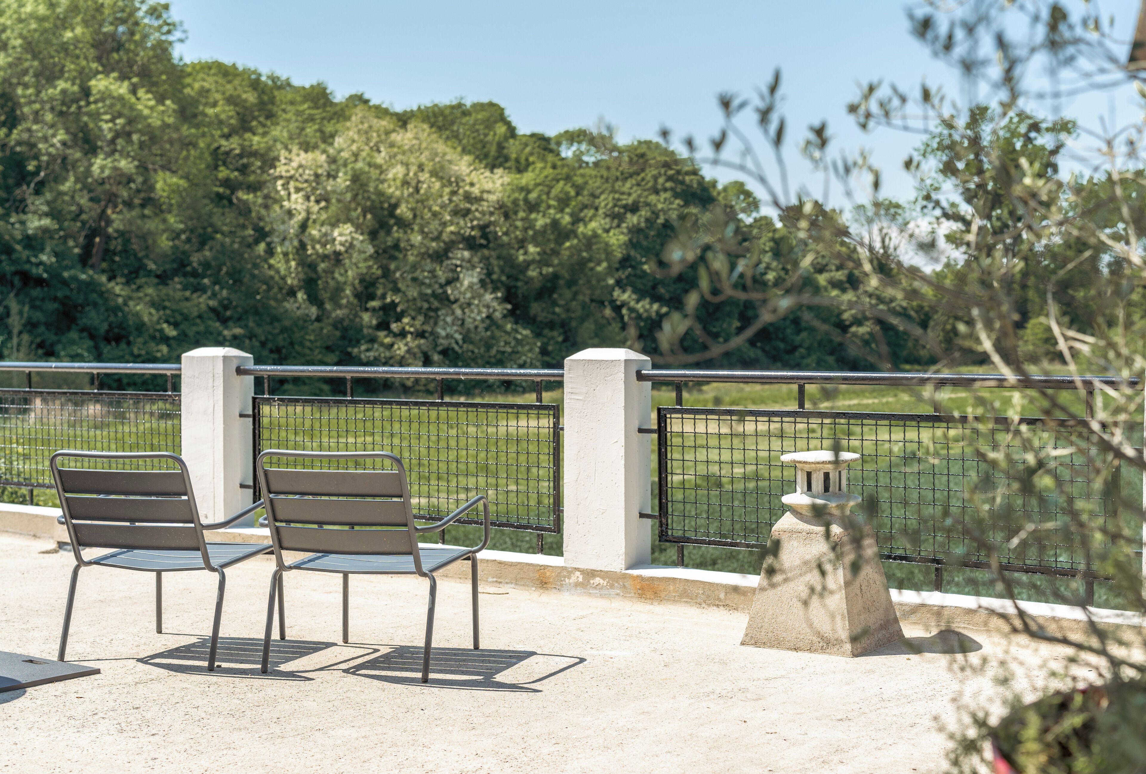 Een zithoek met twee stoelen en een tafel, een stenen constructie, en uitzicht op een groen landschap met bomen.