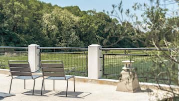 Een zithoek met twee stoelen en een tafel, een stenen constructie, en uitzicht op een groen landschap met bomen.
