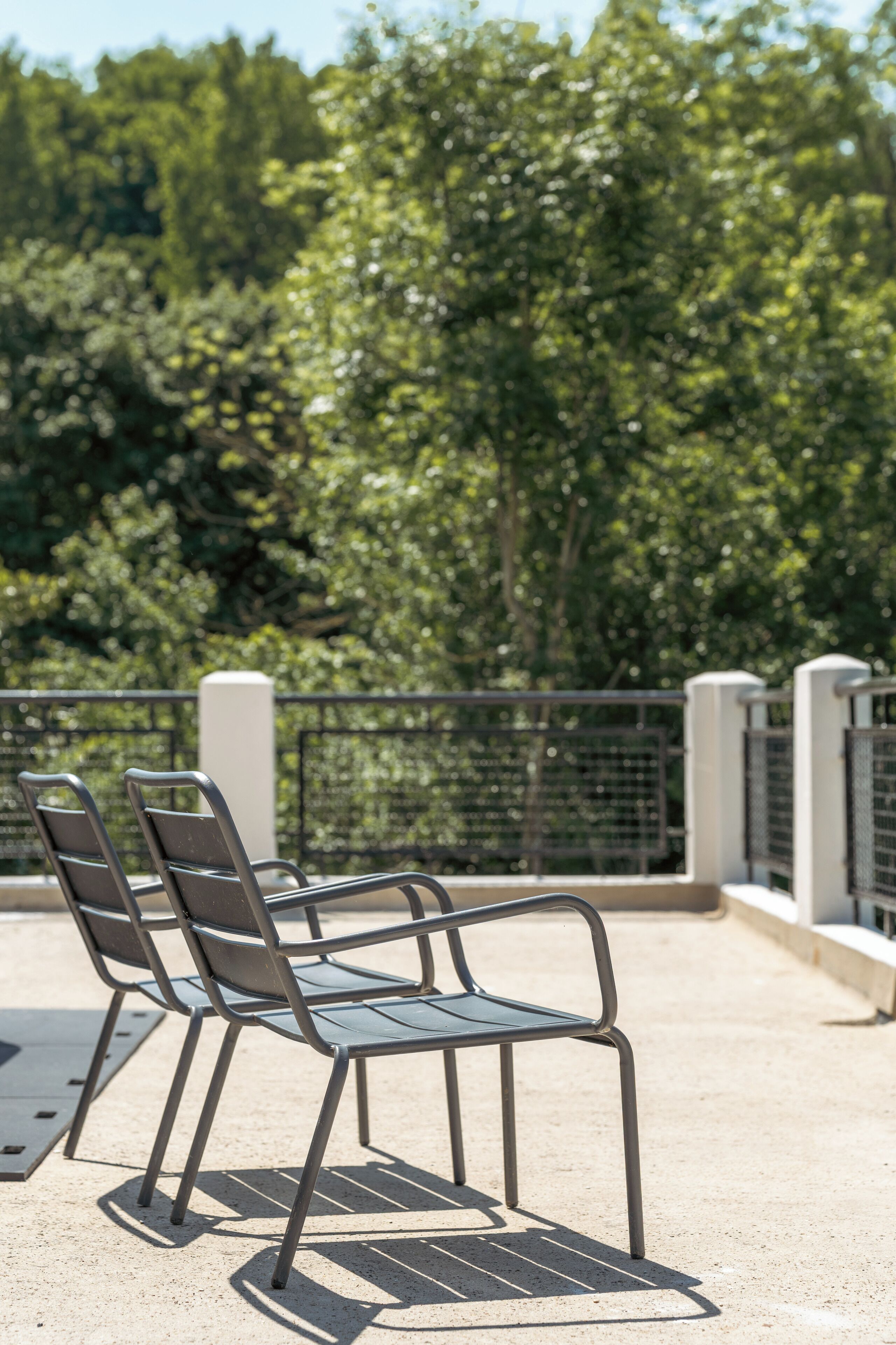 Two metal chairs on a concrete surface with a metal railing and trees in the background.