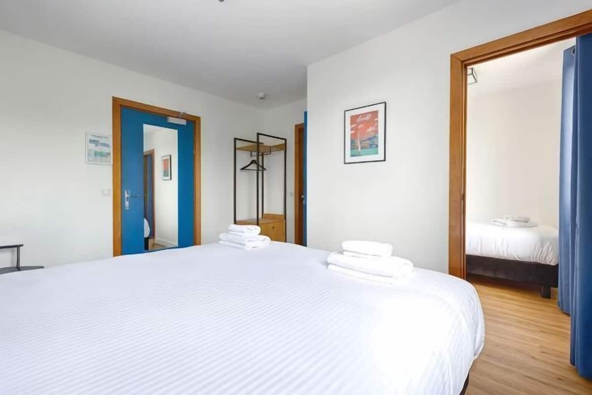 Ein Hotelzimmer mit einem großen Bett, Holzboden, einem Spiegel und einer Tür zu einem anderen Raum.