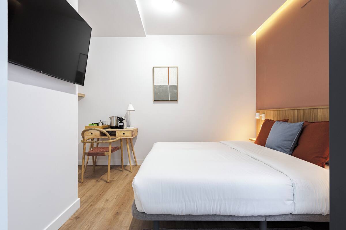 Une chambre d’hôtel moderne équipée d’un lit, d’un bureau, d’une chaise et d’un téléviseur à écran plat.
