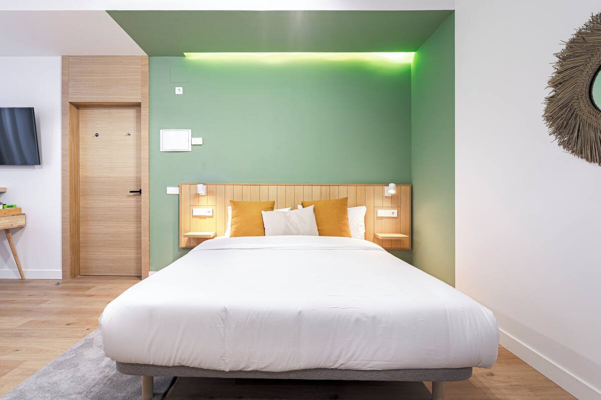 Une chambre moderne avec un grand lit, des murs verts, une tête de lit en bois et des lampes de chevet.