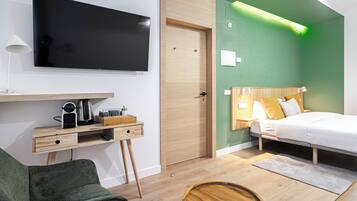 Una habitación de hotel moderna con televisor de pantalla plana, escritorio de madera, paredes verdes y una cama con ropa blanca.