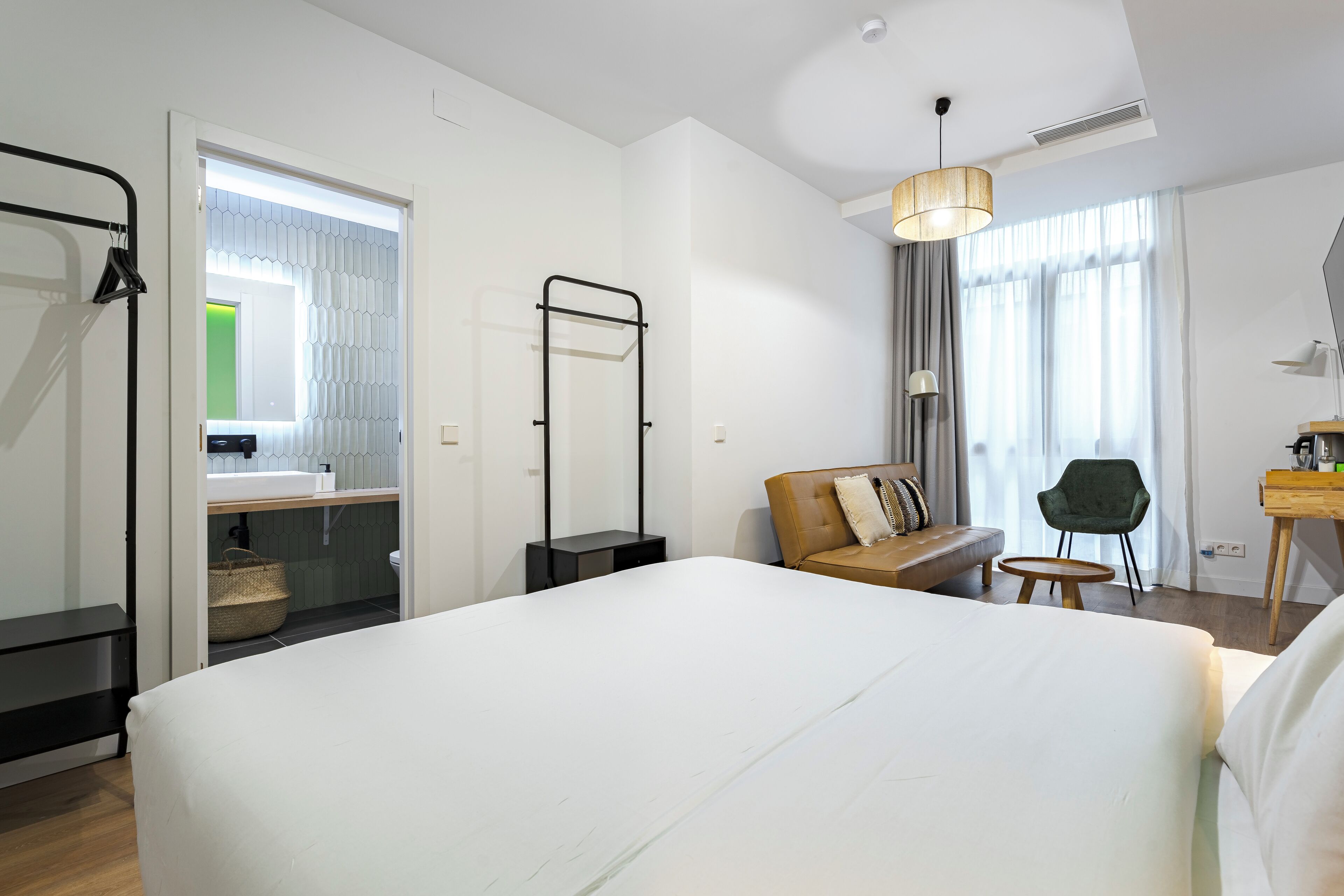 A modern hotel room with a large bed, a desk, a chair, and a sofa.