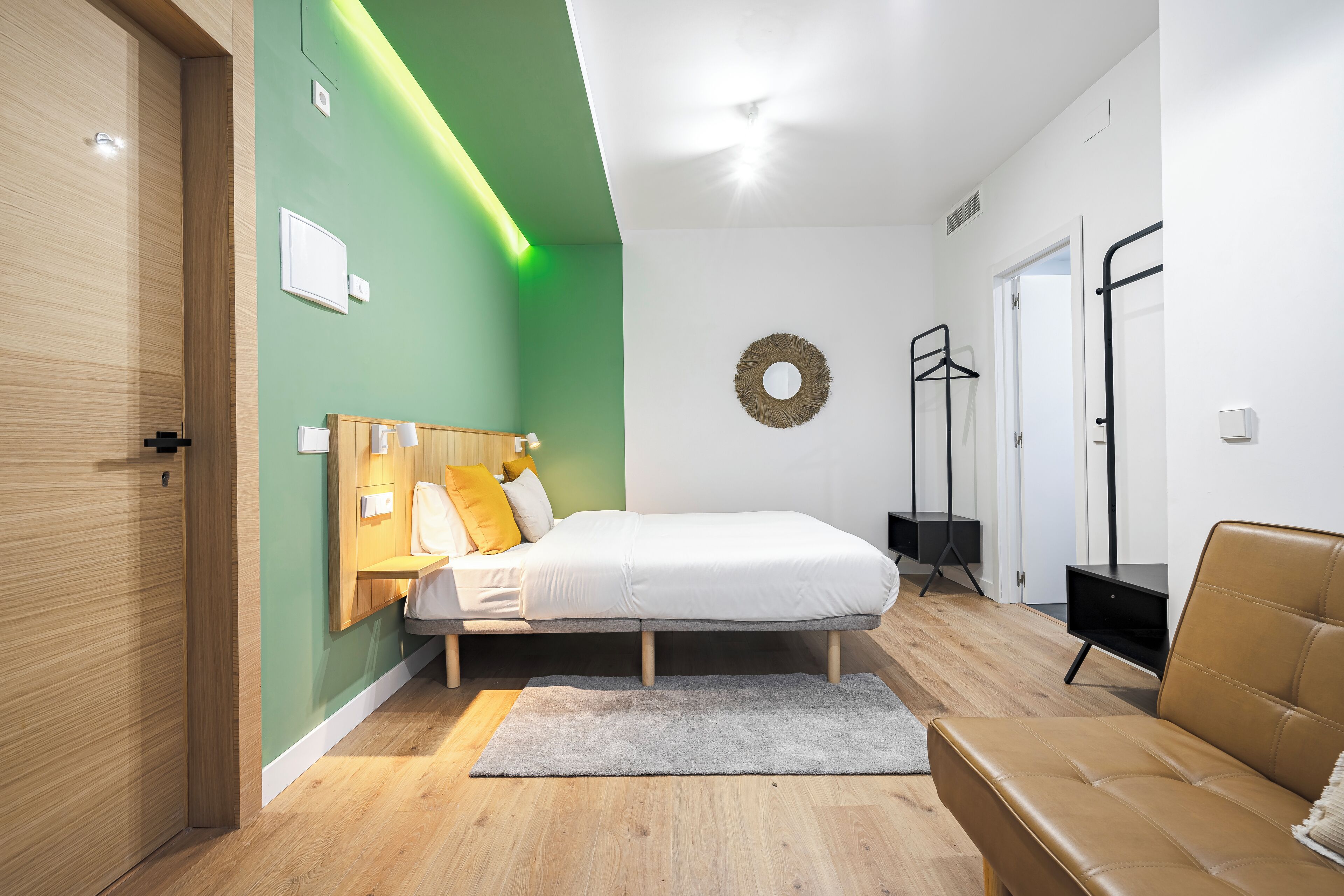 Un dormitorio moderno con cama, armario de madera, alfombra gris y sofá de cuero marrón.
