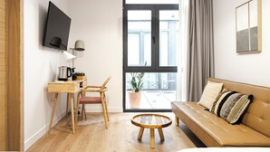 Un salon moderne comprenant un canapé, une table basse, un bureau avec une chaise, un téléviseur fixé au mur et une grande fenêtre avec des rideaux.