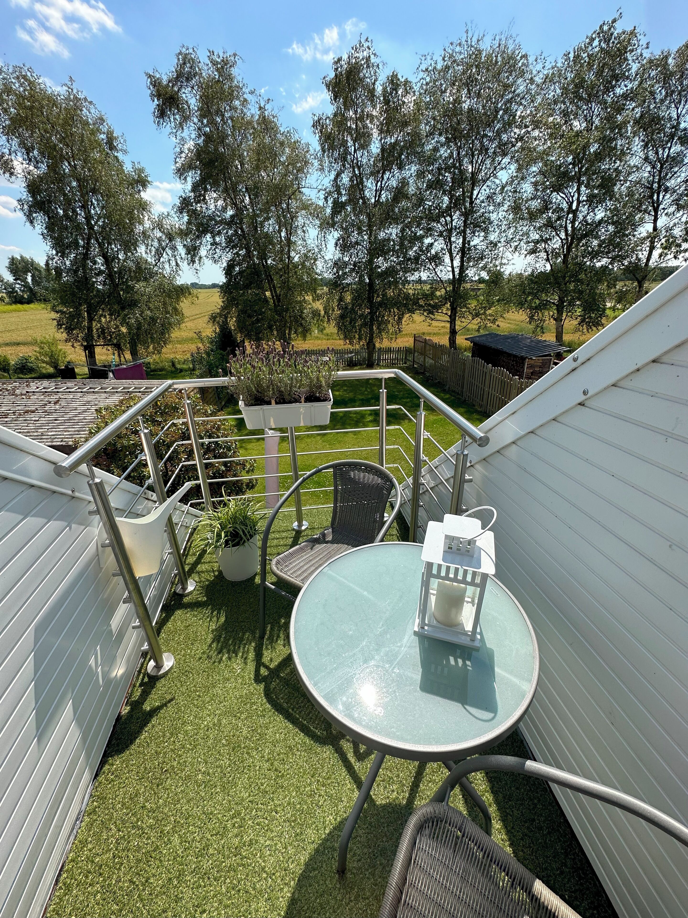 Ein Patio mit einem runden Tisch und Stühlen, einem hängenden Blumentopf mit Pflanzen und Blick auf die umliegende Landschaft.