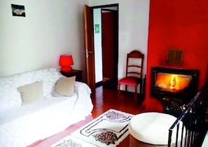 Een kamer met een witte bank, een rode muur, een open haard en een deur naar een andere kamer.