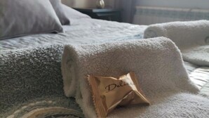 A neatly made bed with a rolled towel and a packet labeled "Deluxe" on it.