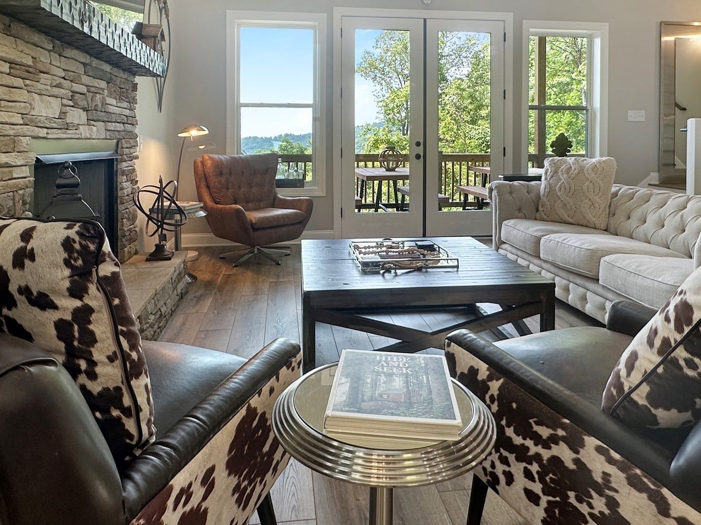 A living room with a stone fireplace, leather armchairs, a coffee table, and a view through large glass doors.