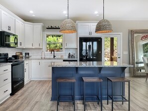 A modern kitchen with white cabinets, a black refrigerator, and a blue island with bar stools. - Mountain-view cabin with hot tub, game room, and 3 bedrooms. Free rafting, train, zip (Bryson City)