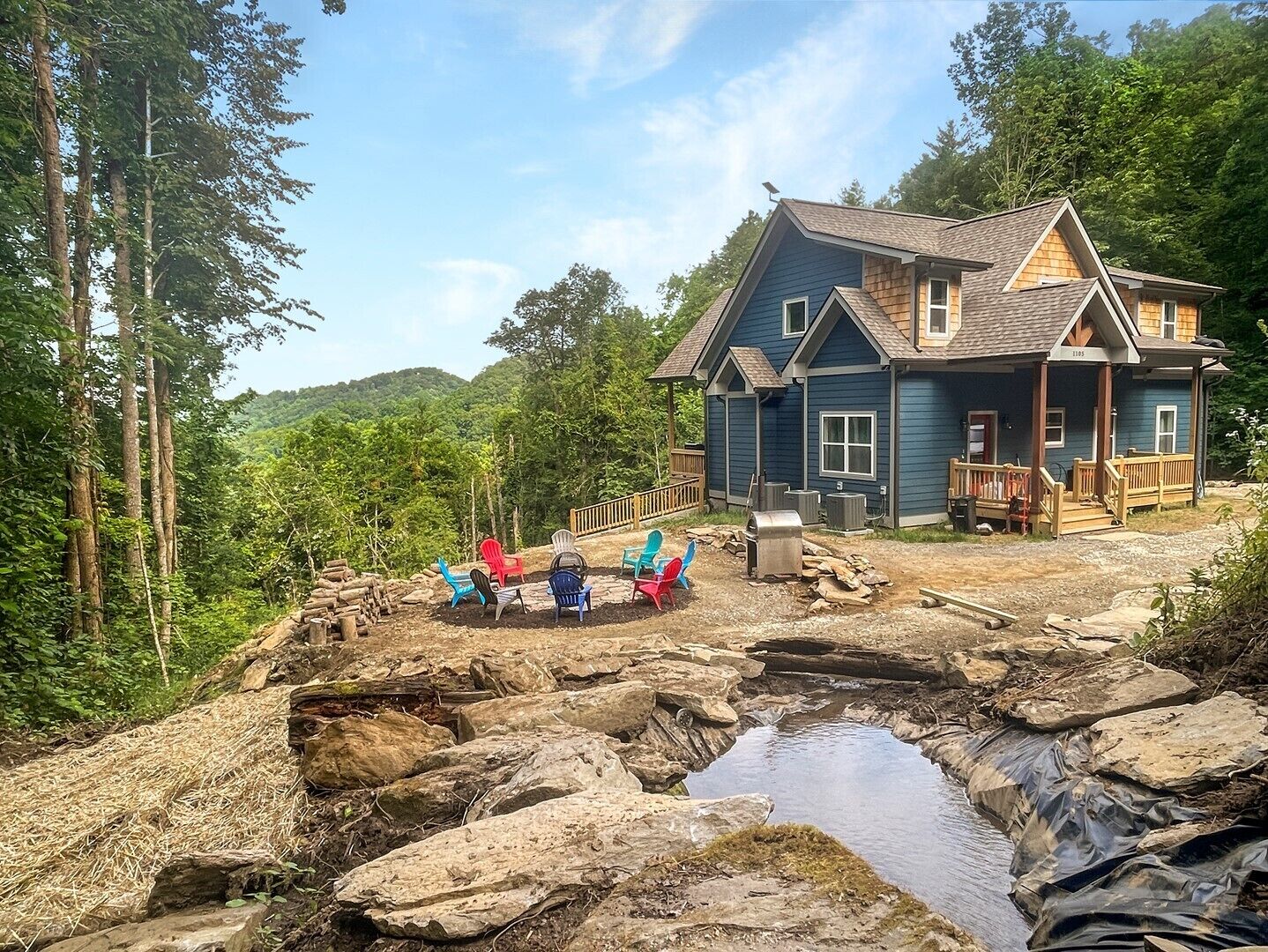 Eine rustikale Holzhütte mit Veranda, eingebettet in eine natürliche Landschaft mit Bäumen und einem kleinen Bach.