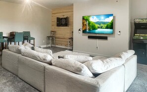 A living room with a large sectional sofa, a flat-screen TV mounted on the wall, and a dartboard. - Mountain-view cabin with hot tub, game room, and 3 bedrooms. Free rafting, train, zip (Bryson City)