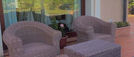 A patio area with wicker furniture and a glass door leading to a garden.