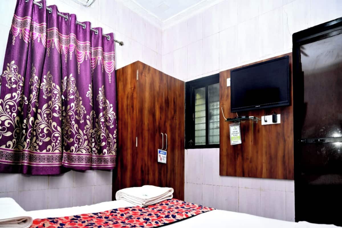 A hotel room with a bed, a TV mounted on the wall, a wooden wardrobe, and purple curtains.