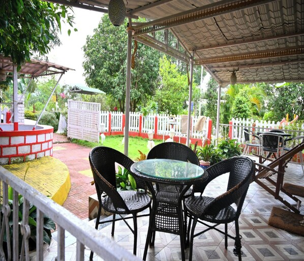 An outdoor patio with a round glass table and wicker chairs, surrounded by a white picket fence and greenery. - KK Tree Retreat (Igatpuri)