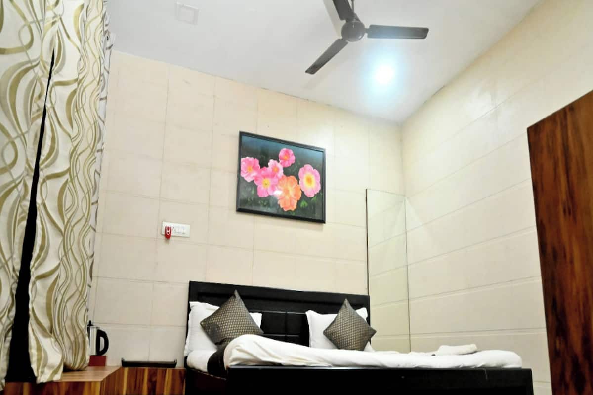 A bedroom with a bed, a ceiling fan, a wall-mounted painting of flowers, and a wooden wardrobe.