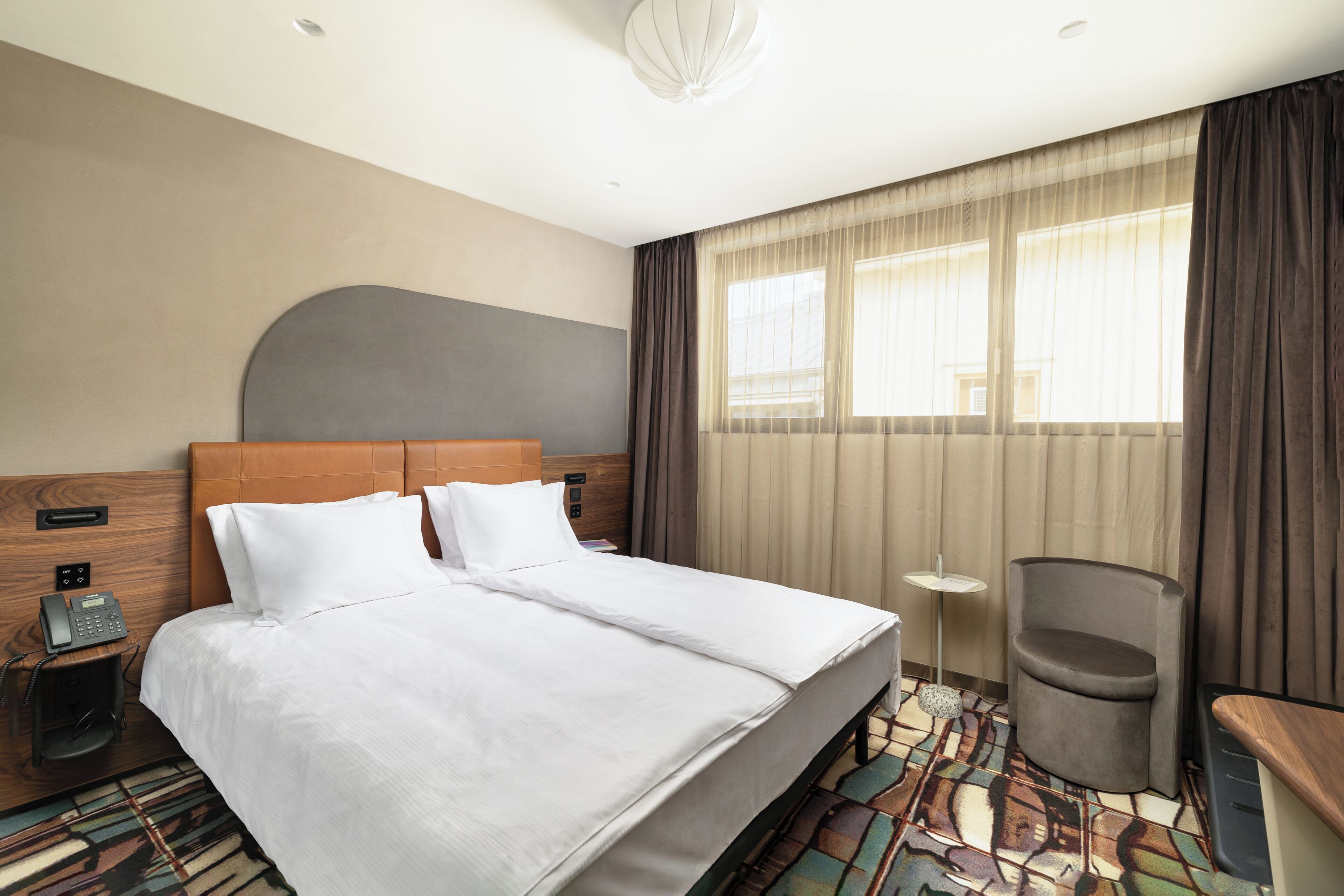 Une chambre d’hôtel avec un lit double, un bureau, une chaise, un téléphone et une fenêtre avec des rideaux.
