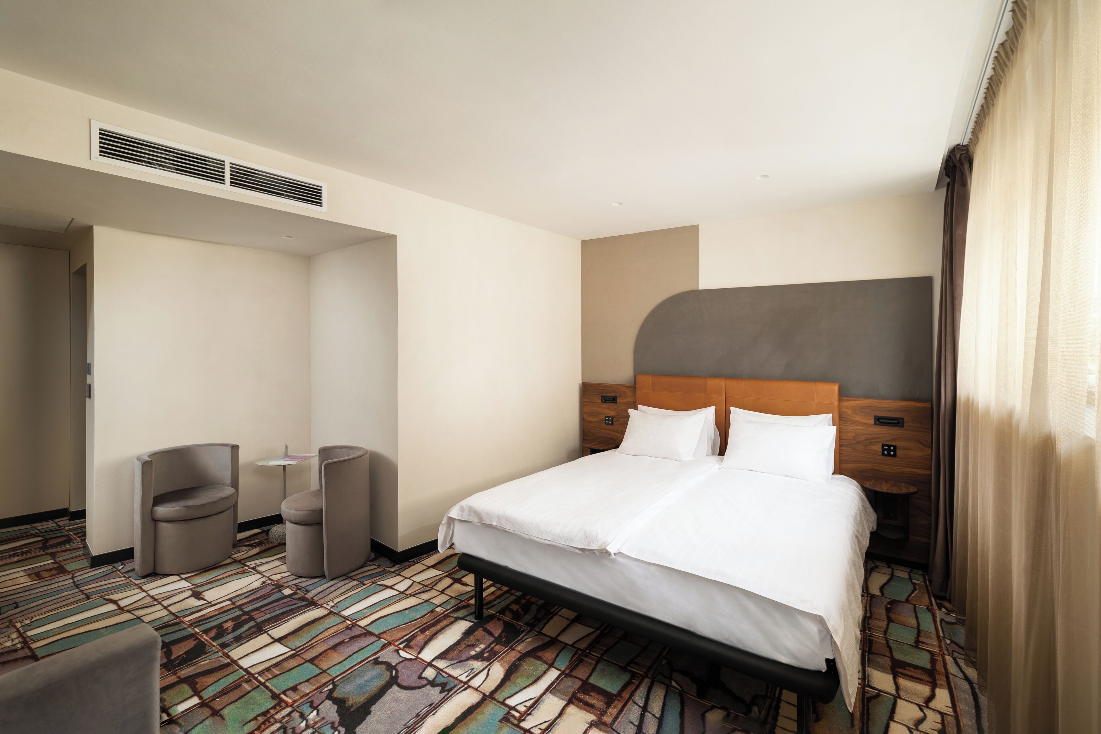 A hotel room with a bed, two armchairs, a small table, and a patterned carpet.