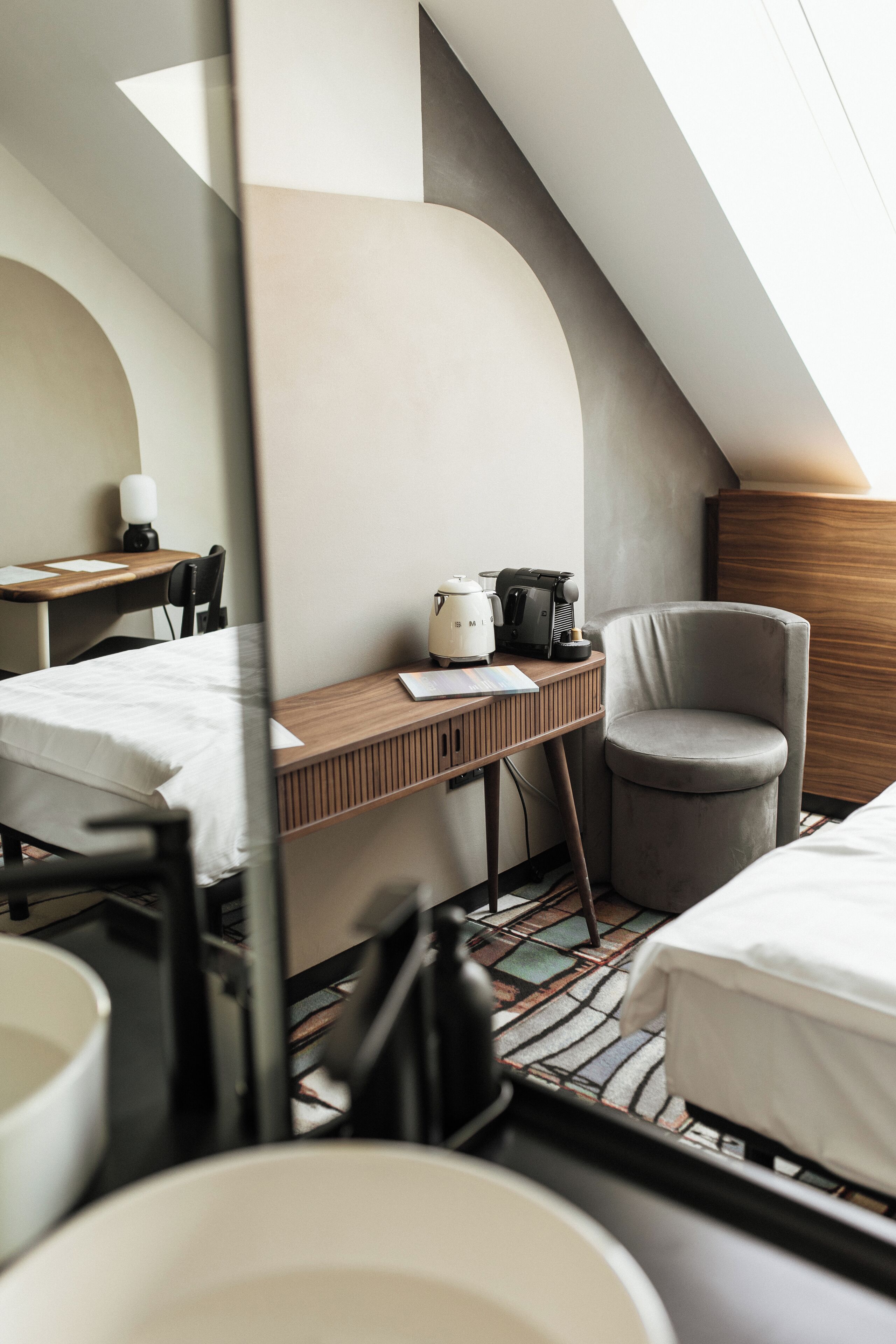 A modern hotel room with a loft bed, a desk with a laptop, a chair, and a coffee machine.
