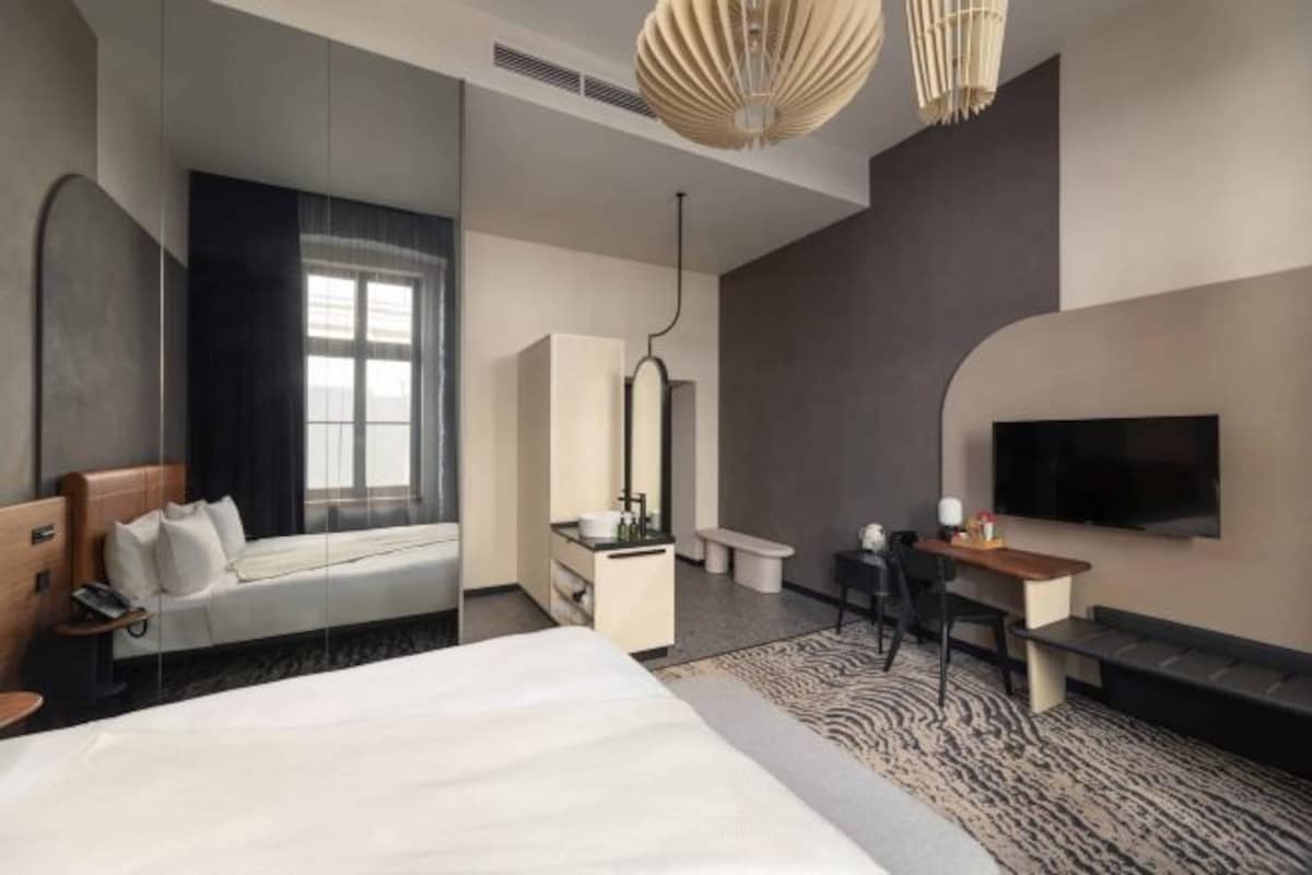 Una habitación de hotel moderna con una cama grande, un escritorio, un televisor y una ventana con cortinas.