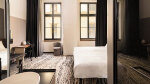 A hotel room with a bed, a desk, a chair, a small table, and two windows with curtains. - Hotel GIN Budapest (Budapest)