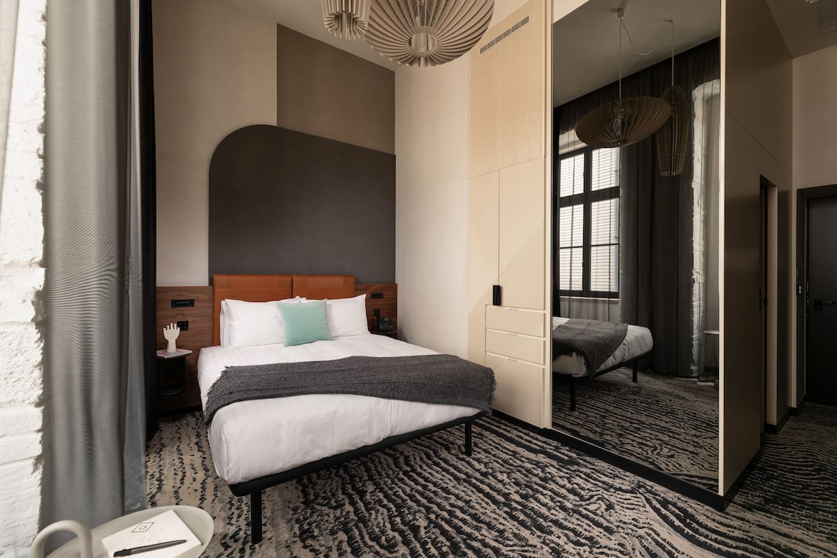 Una habitación de hotel moderna con una cama grande, una mesita de noche, un espejo y una alfombra estampada.