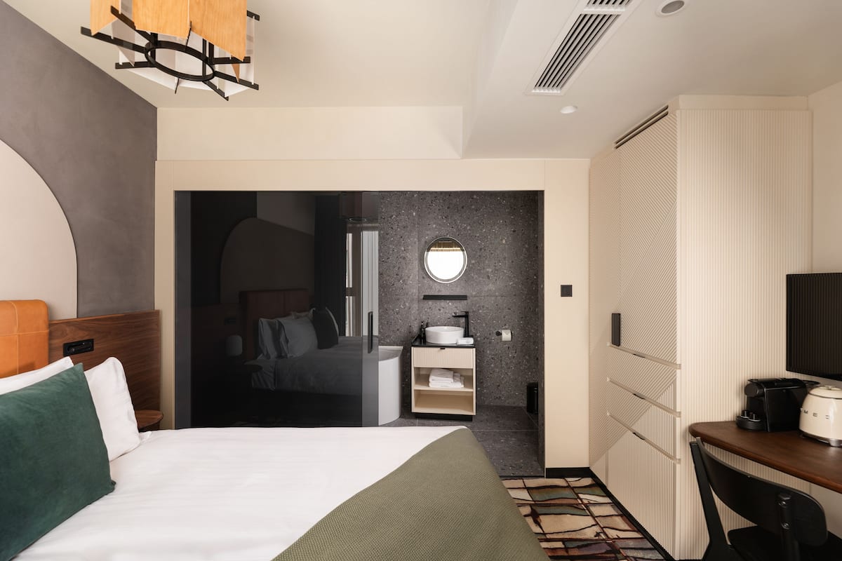 Habitación de hotel moderna con cama, escritorio, baño y vista al pasillo.