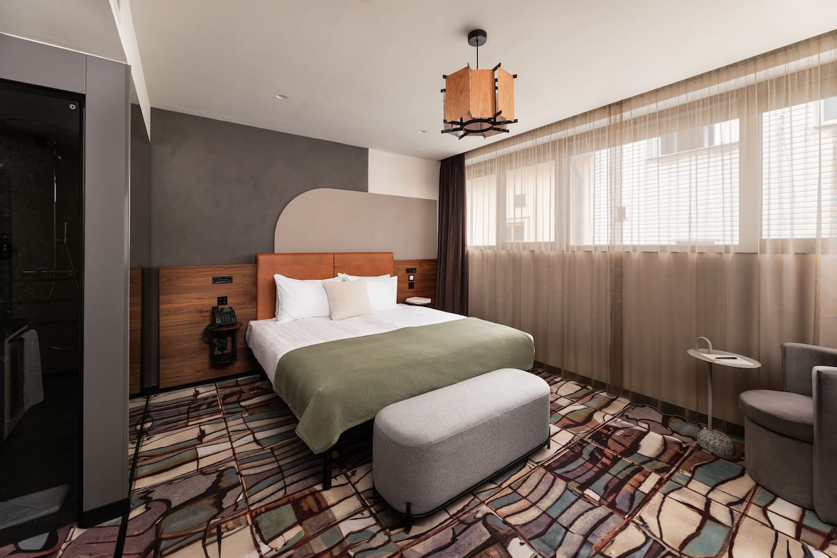 Una habitación de hotel moderna con una cama grande, una mesita, un banco y un área de ducha.